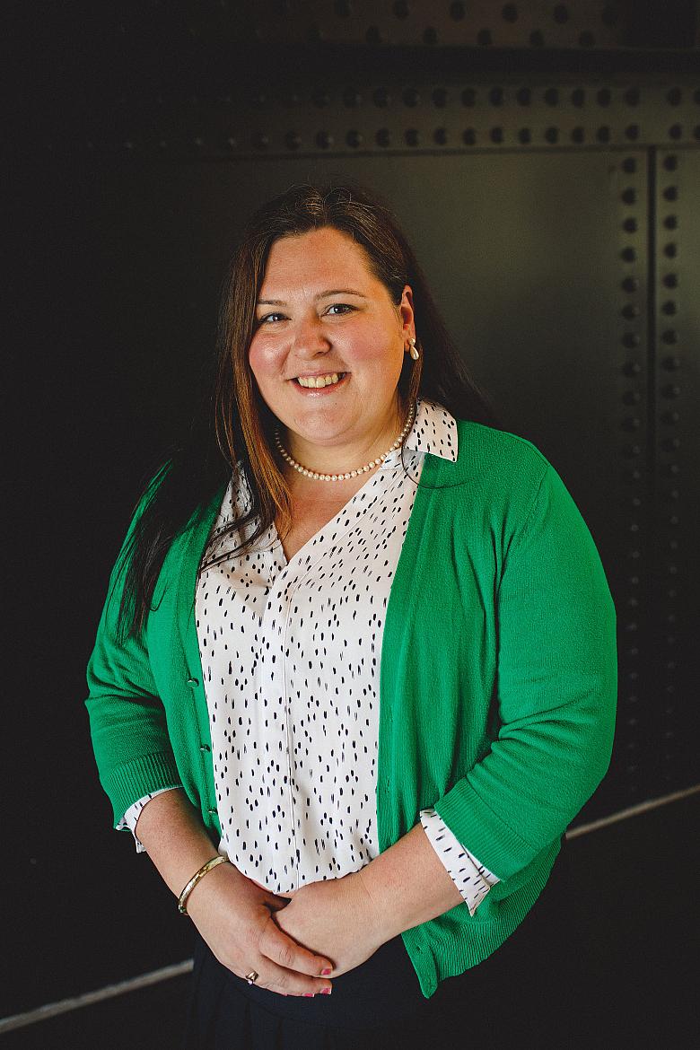 a women in a white shirt and green cardigan looks at the camera